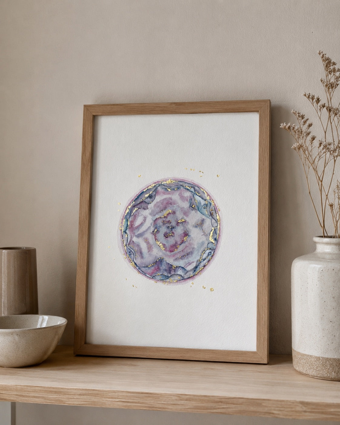 Framed watercolour embryo with a floral design on a wooden shelf against a beige wall.