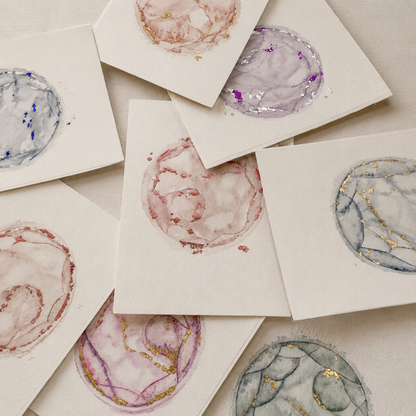 Artistic representations of watercolour embryo designs on small cards with a neutral background