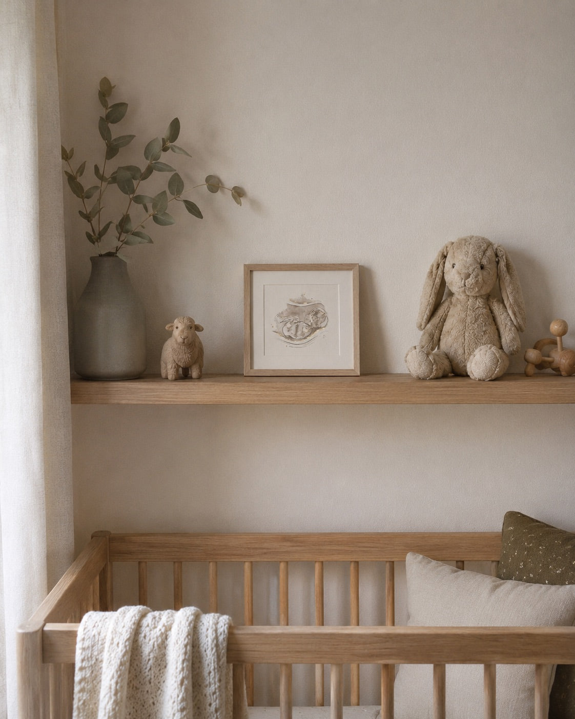 Framed ultrasound/sonogram watercolour painting in a nursery with wooden crib, shelves with toys and decor, and a vase with greenery.